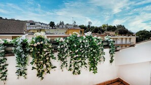 Een terras op het dak, met een witte muur en verschillende bloeiende planten.
