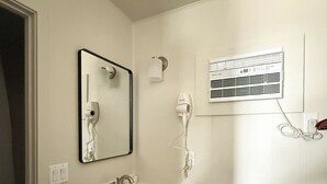 Een moderne badkamer met een wit wastafelmeubel, donkere kastjes, een spiegel, een haardroger en een luchtverfrisser aan de muur.