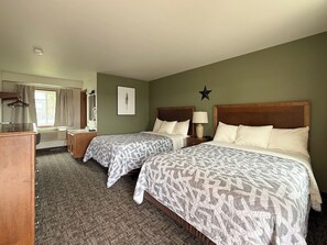 A hotel room with two beds, a desk, a chair, a dresser, a window with curtains, a star decoration on the wall, and a framed picture. -  The Trail Inn & RV Sites - Selby, SD - HWY 12, HWY 83 (Selby)