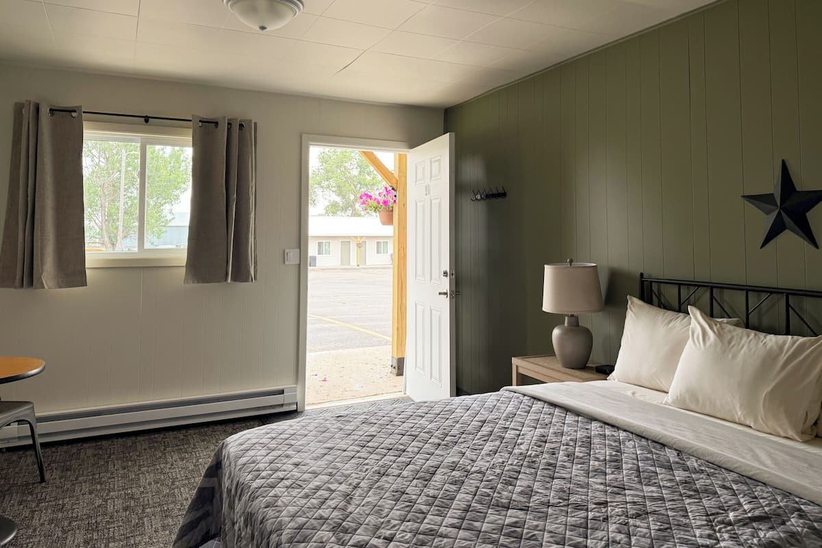A hotel room with a bed, a bedside table with a lamp, a window with curtains, a star decoration on the wall, and a view of the outside.