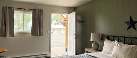 Una habitación de hotel con cama, mesita de noche con lámpara, ventana con cortinas, adorno de estrella en la pared y vista al exterior.