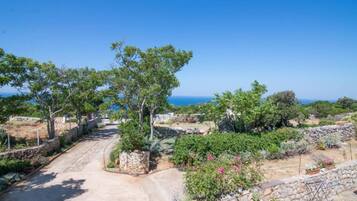 Un sentier qui traverse un jardin bordé de murs de pierre et d’arbres, et d’où l’on a une vue sur la côte.