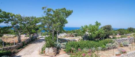 A pathway leading through a garden with stone walls and trees, overlooking a coastal area.