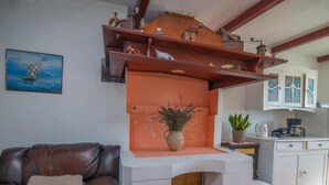 A living room with a brown leather sofa, a white fireplace, a potted plant, and a kitchen area with cabinets and a coffee maker.