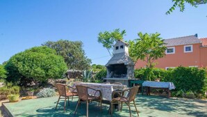 An outdoor patio with a table and chairs, a stone barbecue grill, and a building in the background. - Apartments Bonic - Two Bedroom Apartment (Veli Losinj)