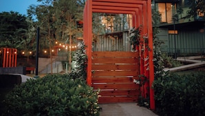 A wooden gate with a red frame, surrounded by greenery and string lights. - Mata e' Platano Guesthouse #4, Luquillo PR (Luquillo)