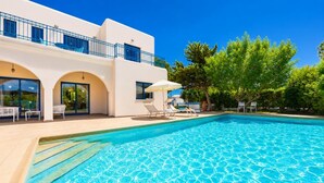 A swimming pool with lounge chairs, a covered area, and a building with balconies and large windows.
