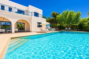 Una piscina con lettini, una zona coperta e un edificio con balconi e ampie finestre.