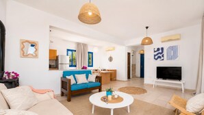 A modern living room with a sofa, coffee table, and TV. There is a kitchen area with a dining table and chairs.
