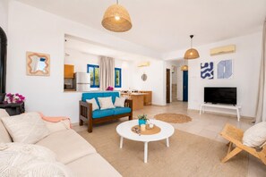 A modern living room with a sofa, coffee table, and TV. There is a kitchen area with a dining table and chairs.