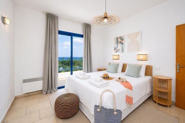 Ein Hotelzimmer mit einem großen Bett, Meerblick, einem runden Hocker und einem Holztischchen.