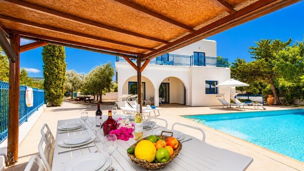 A covered outdoor dining area with a pool and a white building in the background.