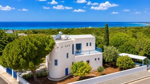 A white building with a blue balcony, solar panels, and a view of the sea.