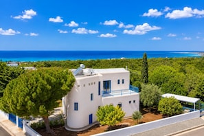 Un edificio bianco con un balcone blu, pannelli solari e vista mare.