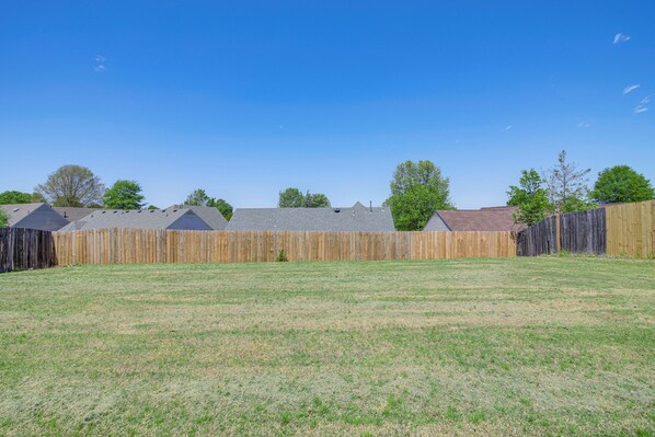 A fenced backyard with a grassy lawn and a wooden fence. - Large Backyard: Peaceful Home in Southaven! (Southaven)