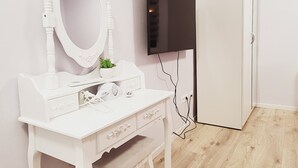 Une coiffeuse blanche avec un miroir, une petite plante et un téléviseur à écran plat fixé au mur.
