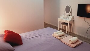 Une chambre à coucher moderne avec un lit, des oreillers, une coiffeuse avec un miroir et un téléviseur fixé au mur.