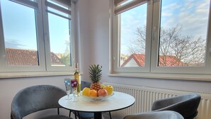 Un coin repas avec une table ronde, deux chaises, un panier de fruits, une bouteille et un verre.
