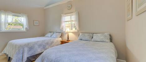 A bedroom with two beds, each with a white quilted bedspread, a bedside table with a lamp, and a window with white curtains.