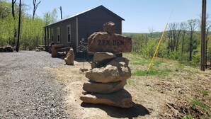 A rustic cabin with a gravel driveway, a stack of rocks with 'ZEN DEN' carved on it, and a bicycle leaning against the cabin.