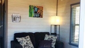 A dark-colored sofa with floral-patterned cushions, a wall-mounted lamp, and a colorful abstract painting above it.