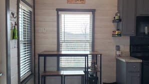 A kitchen with wooden walls, a window with blinds, a table with chairs, and a microwave.