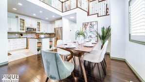 Eine geräumige Küche mit weißen Schränken, ein Essbereich mit einem Holztisch und eine Treppe, die zu einer oberen Ebene führt.