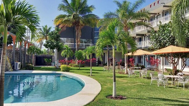 A pool surrounded by palm trees and a building with balconies. - Villa Salvatore (Xochitepec)