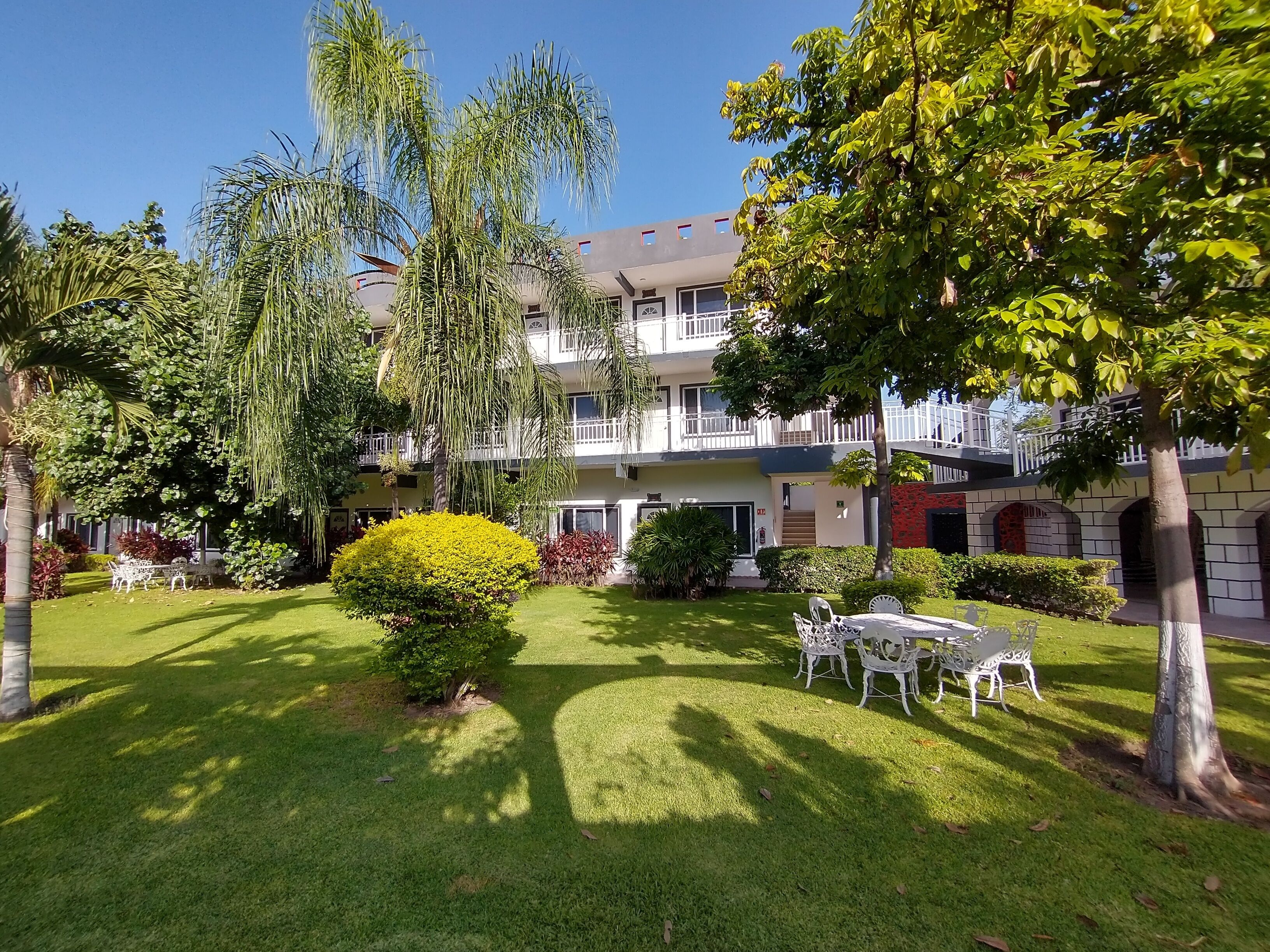 A multi-story building with a well-maintained garden, outdoor seating, and a clear sky.