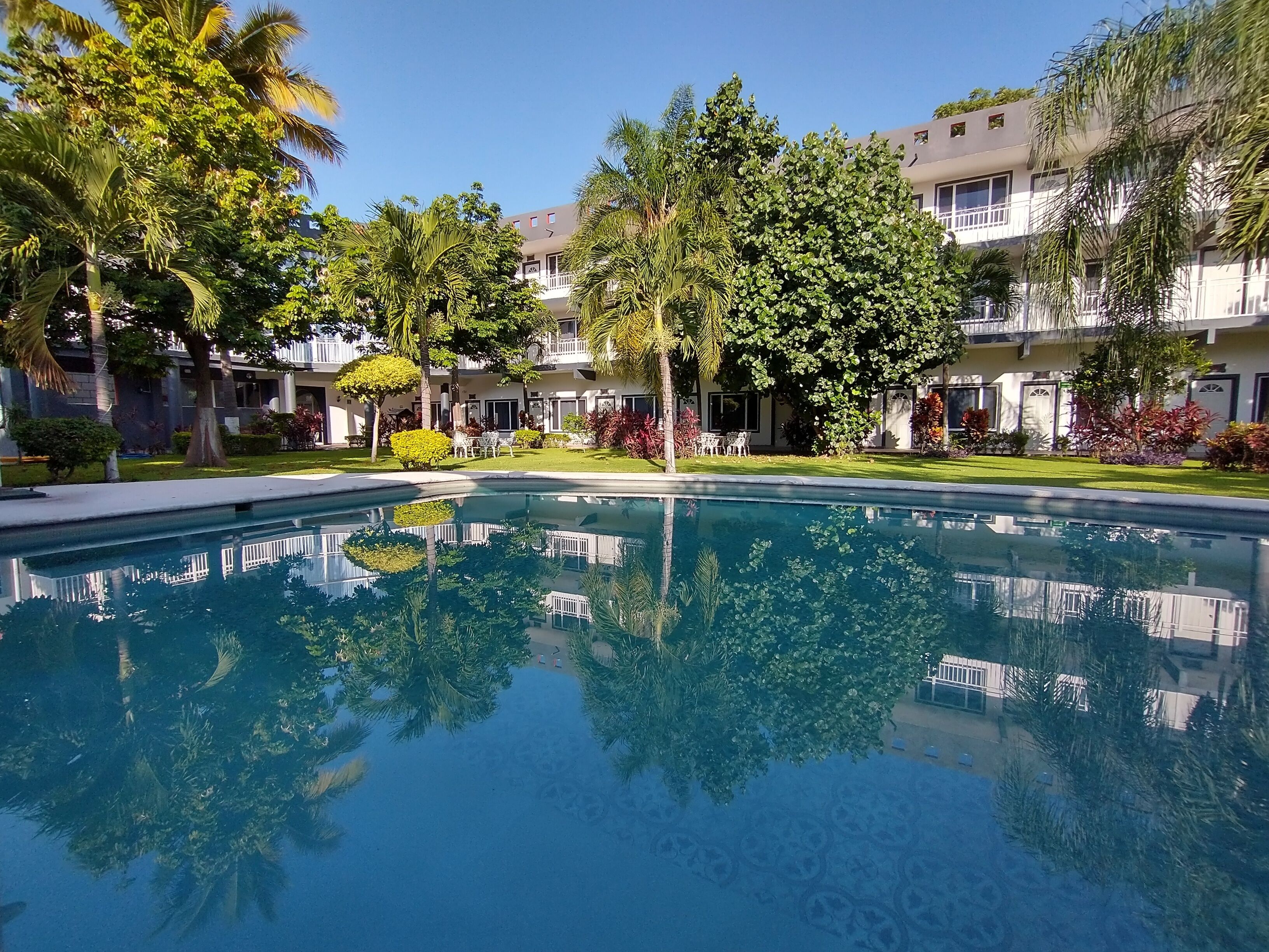 A pool surrounded by lush greenery and a multi-story building with balconies.