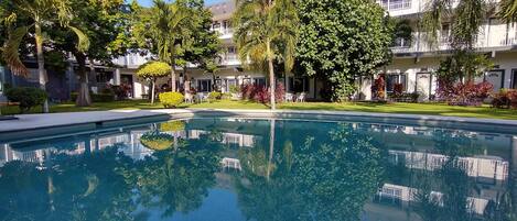 A pool surrounded by lush greenery and a multi-story building with balconies.
