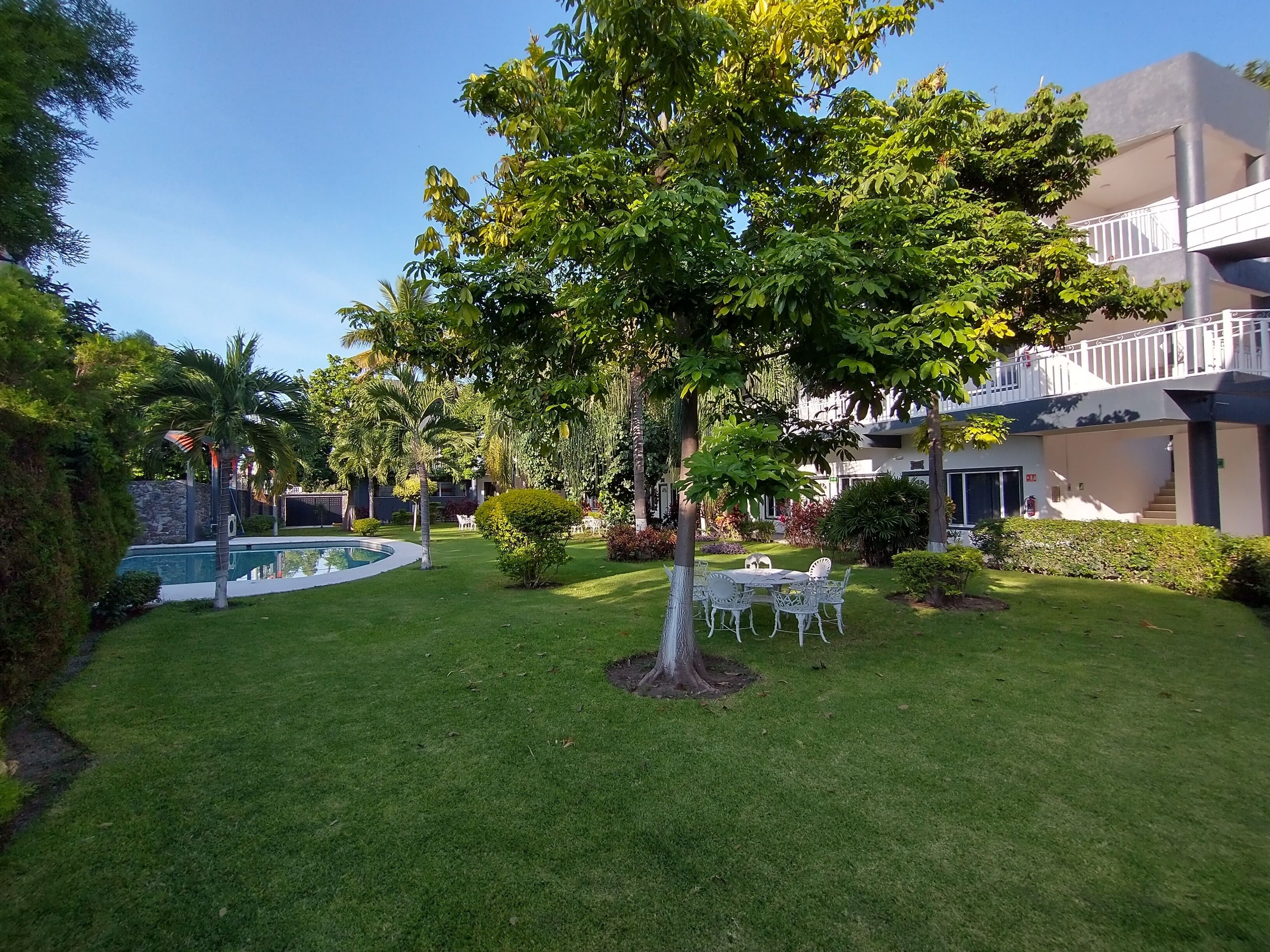 A well-maintained garden with a pool, outdoor seating, and a building with a balcony.