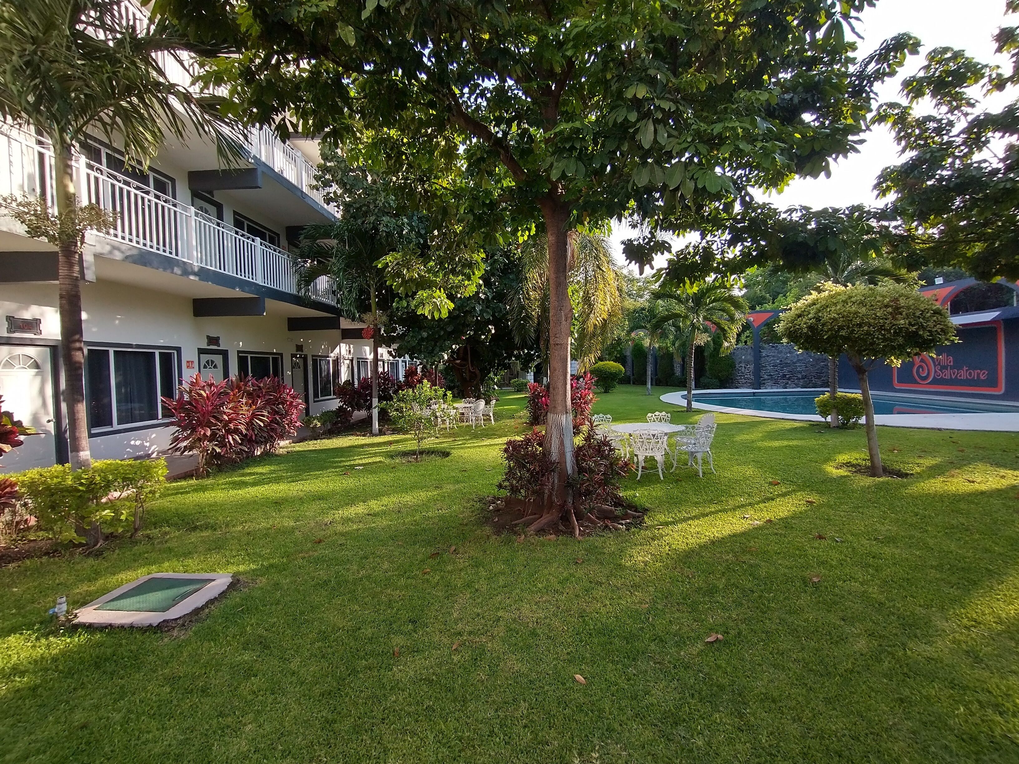 Un jardín bien cuidado con piscina, mobiliario exterior y un edificio con balcones.