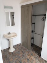 Un baño con lavamanos pedestal, un espejo, una puerta de madera y una zona de ducha.