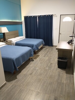 Habitación de hotel con dos camas, un escritorio, un cubo de basura, una lámpara y una ventana con cortinas.