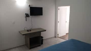 A bedroom with a bed, a desk with a computer, a TV, and a door.