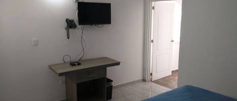 Un dormitorio con cama, escritorio con computadora, televisor y una puerta.