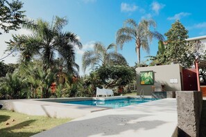 Una piscina rodeada de palmeras y follaje, con un edificio moderno al fondo.