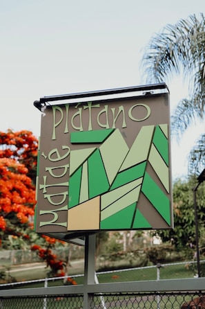 Un letrero con el nombre 'Platano' y algo de texto en un idioma extranjero.