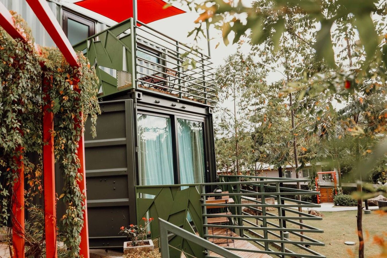 Un edificio moderno con fachada verde, una escalera que lleva a un balcón y vistas a un jardín.