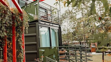 Un edificio moderno con fachada verde, una escalera que lleva a un balcón y vistas a un jardín.