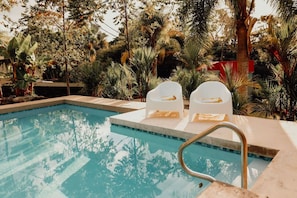 Ein Swimmingpool mit zwei weißen Liegestühlen und einer Metallleiter.