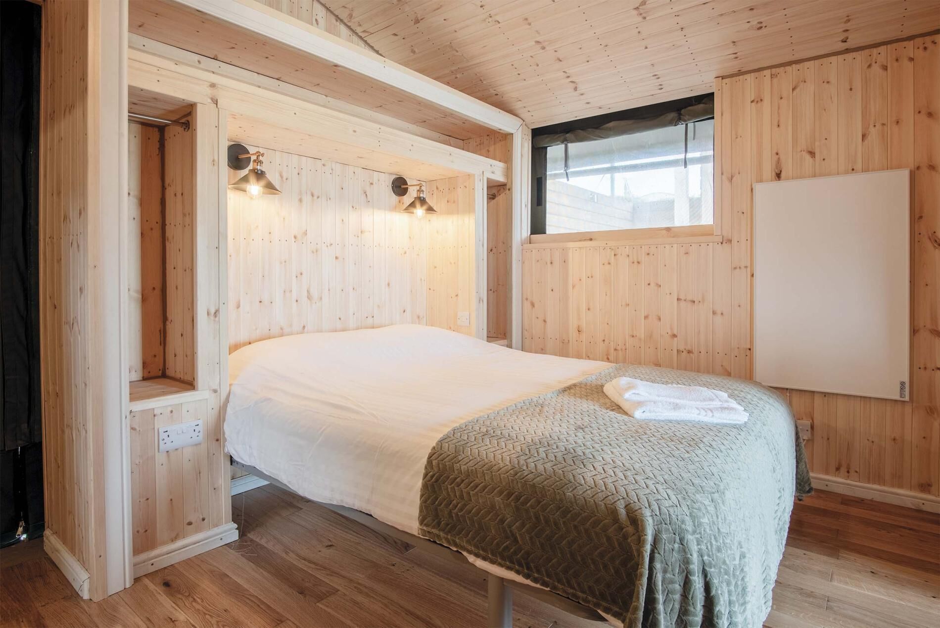 A wooden-paneled bedroom with a bed, two wall-mounted lamps, and a window.
