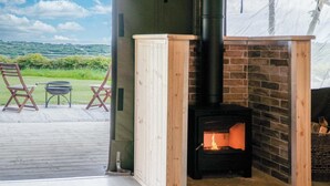 A wood-burning stove in a corner of a room with a view of a green landscape. - Paviland - Safari Glamping Tent - Llangennith (Llangennith)