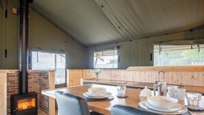 A cozy cabin interior with a brick fireplace, wooden dining table, and comfortable seating. - Paviland - Safari Glamping Tent - Llangennith (Llangennith)