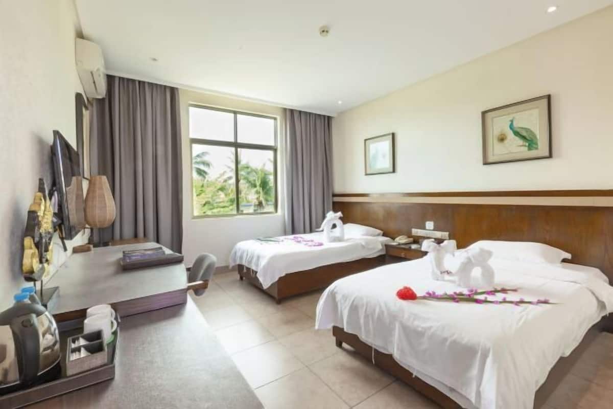 Quarto de hotel com duas camas, uma mesa, uma televisão e uma janela com cortinas.