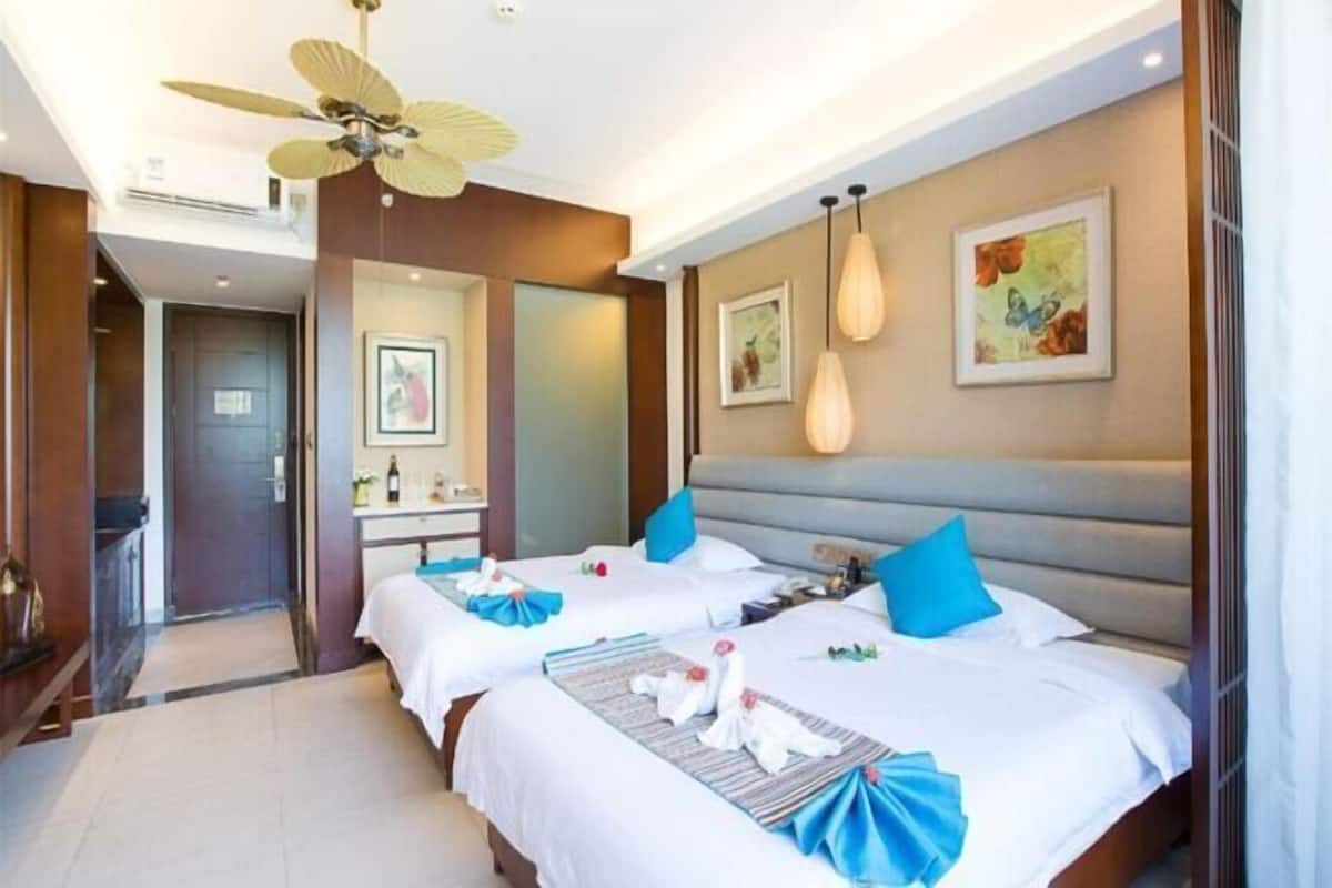 Quarto de hotel com duas camas, ventoinha no teto, obras de arte nas paredes e banheiro com espelho e pia.