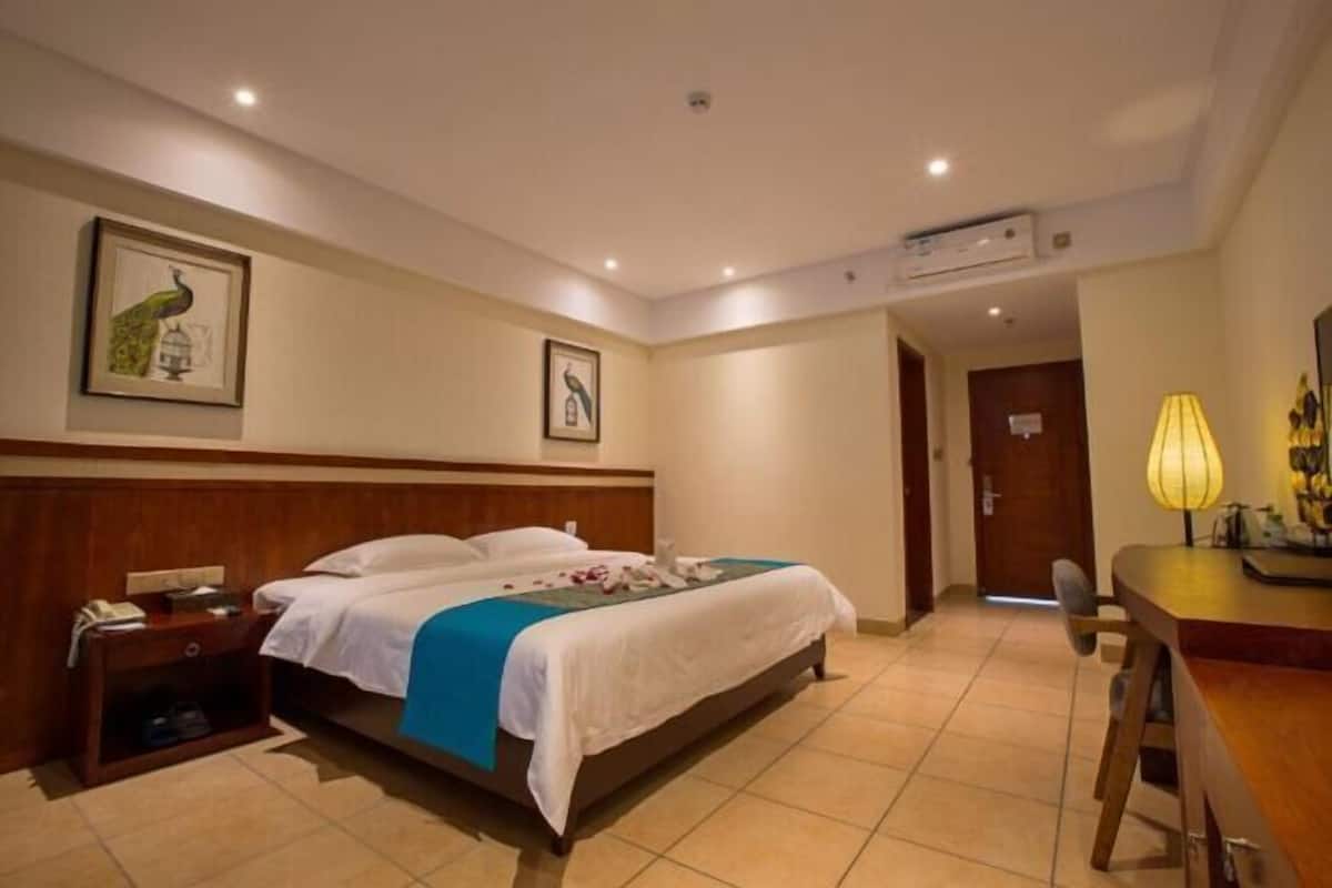Quarto de hotel com uma cama grande, uma escrivaninha com abajur e duas molduras na parede.