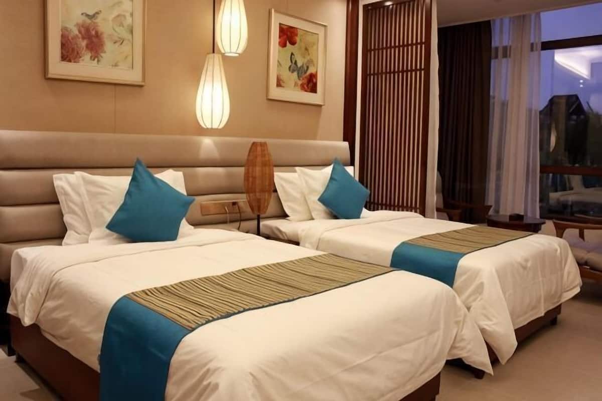 Quarto de hotel com duas camas, uma janela grande e obras de arte nas paredes.
