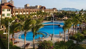 A resort with a central swimming pool, palm trees, and a view of distant mountains. - Longxing Lehman Sea View Resort (Sanya)